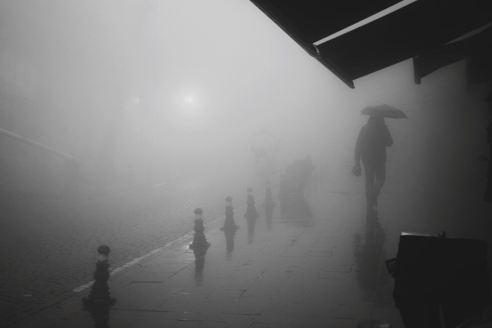 Regennasse, neblige Straße mit einer silhouettierten Person unter Schirm