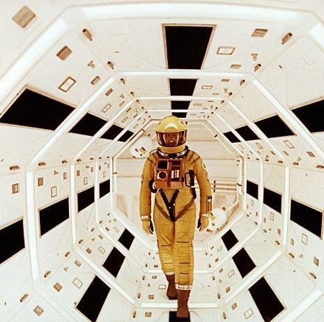 Astronaut in orangefarbenem Raumanzug auf einem weißen Raumschiffkorridor